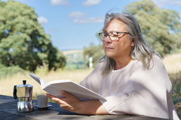 a woman reads a book  in a field while drinking a cup of coffee.