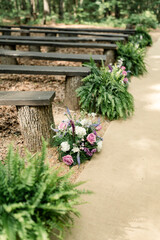 Floral arrangements and benches along an outdoor wedding aisle