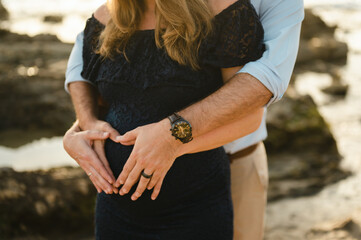 Close up of couple making heart shape with hands over baby bump
