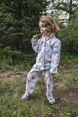 Cute child in pajamas brushing her teeth outdoors in nature