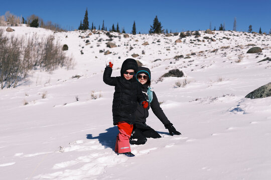 Mother and child playing in snowy landscape with mountains in ba