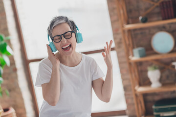 Photo of pretty retired woman sing headphones listen music wear white outfit home flat rest relax...