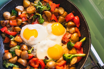 Close-up of a pan with fried eggs, potatoes, broccoli, and red peppers
