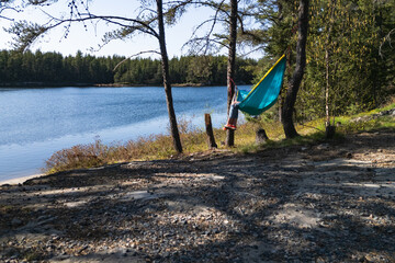 A woman relaxing in a hammock tied between trees by the lake