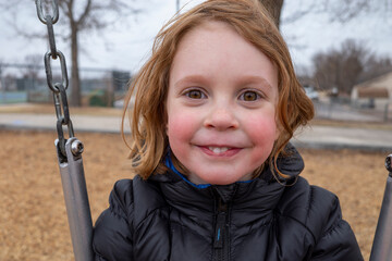 Smiling child on a swing in a winter park