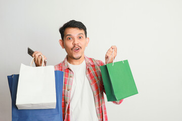 portrait of happy smiling handsome Asian man carrying shopping bags and his smartphone. Online shop concept.