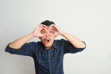 portrait of excited Asian man shocked gesture with both hands pretending to wear glasses