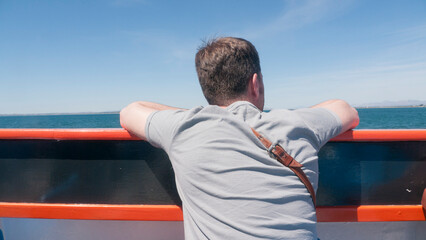 Hombre blanco de espaldas mirando el mar desde la cubierta de un ferry