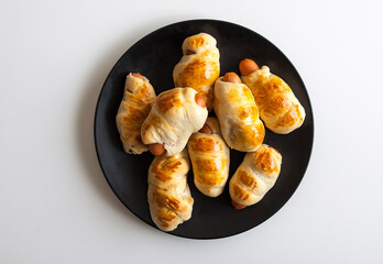 Sausages in the dough on ceramic plate on the table.