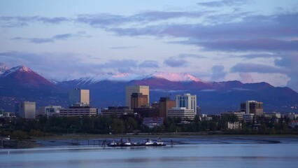 Drone footage of Anchorage city skyline with snowy mountain in the background of sea water at sunset