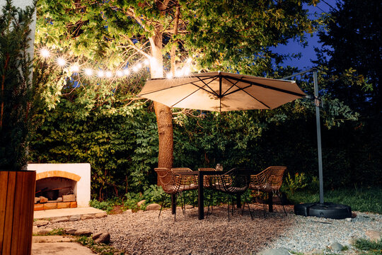 Outdoor patio with table, chairs, and umbrella illuminated by string lights