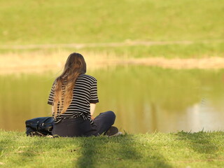 A young girl meditates on the river bank sitting on green grass. Peace of mind and emotional...