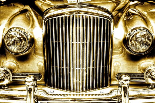 the front end of an antique gold car with chrome grilles
