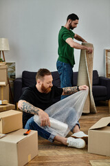 A man sits in front of a large pile of boxes, surrounded by his soon-to-be-unpacked belongings,...