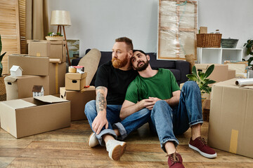A loving gay couple takes a break amid moving boxes, sitting in a cozy embrace on the wooden floor...