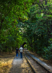 Fototapeta premium two people walking on a train track surrounded by trees, a person carrying an umbrella