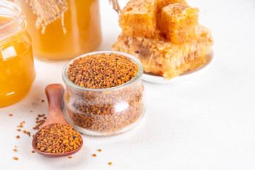 Bee pollen jar and spoon with honey and honeycomb. Trendy superfood, antioxidant organic powder, on white table background copy space