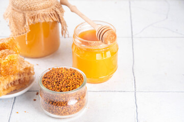 Bee pollen jar and spoon with honey and honeycomb. Trendy superfood, antioxidant organic powder, on white table background copy space