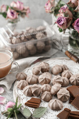 Chocolate meringues, zephyr, on lace napkin with cup of coffee and rose flowers on light background. Sweets, dessert and pastry, homemade cakes, top view