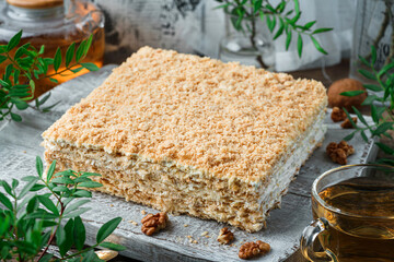 Layered Napoleon cake with cream and nuts on light background with cup of tea and plants. Sweets, dessert and pastry, millefeuille cake, top view, close up