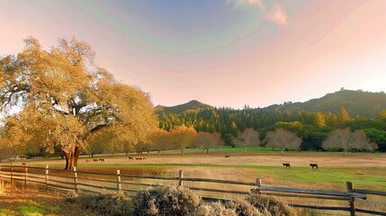 Fototapeta premium A group of cows grazing on a green field near a wooden barrier and tall tree