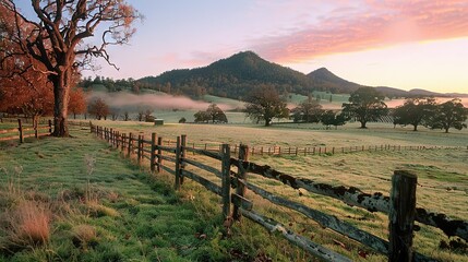  A field with a fence separating it from a tree on one side and a mountain in the background
