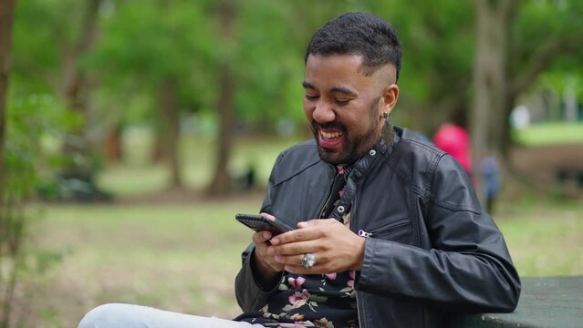 Queer happy guy laughs watching funny video on smartphone looking at phone screen browsing web page on social network young man typing sms on dating site remote chat using virtual
