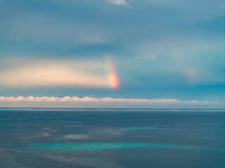 Rainbow over the ocean with blue sky and distant clouds