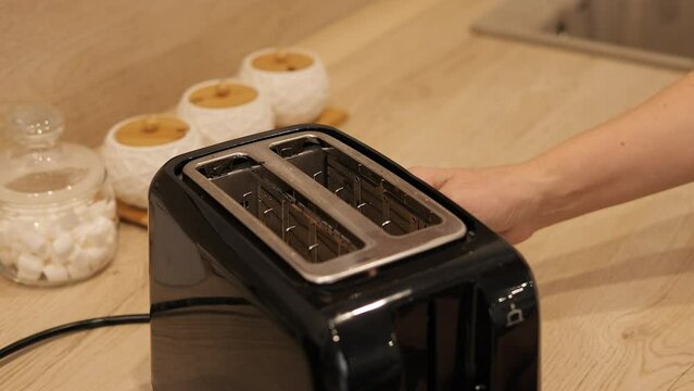 Woman placing bread into toaster Morning routine with toaster making breakfast easy and quick Perfect for kitchen scenes, breakfast preparation, and home appliance use. Focus on toaster and simplicity
