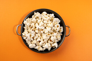Orange background with a black bowl of popcorn.