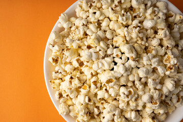 White bowl of popcorn on an orange table.