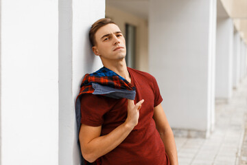handsome fashionable man with a shirt and a red tank top stands near a white building