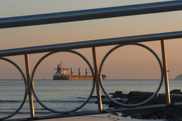 Santos city, Brazil. Water channel n&ordm;6 on the beach during sunset. Cargo ship on the horizon. In the foreground the handrail railing of the bridge over the water channel. 
