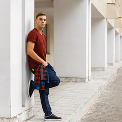 handsome fashionable man with a hairstyle in fashion denim clothes stands near a white building