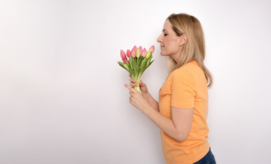 Young blonde woman posing isolated over white wall background holding flowers