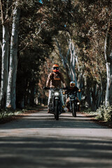 people riding their motorcycles down the street with trees and plants behind them