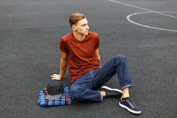 handsome young hipster man in fashionable clothes with a T-shirt and jeans sits in a stadium on the...