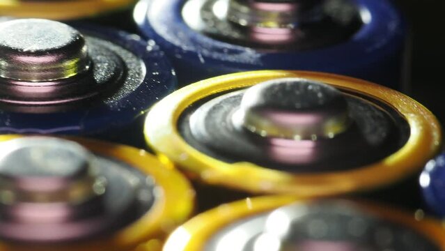 Macro shot of the positive ends of blue and yellow-colored batteries on a rotating platform.