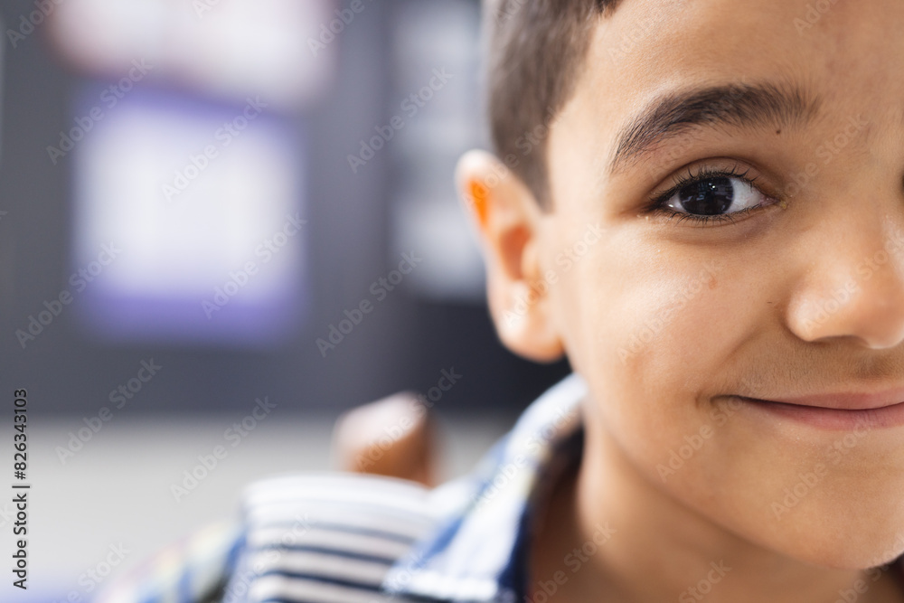 Wall mural In school, in the classroom, a young biracial boy with a cheerful expression is looking forward with