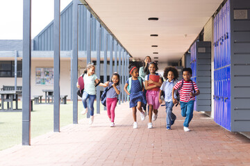 In school, a diverse group of students are running down a hallway outdoors
