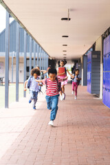 In school, diverse children are running down the hallway with copy space outdoors