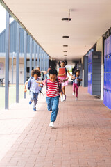 Obraz premium In school, diverse children are running down the hallway with copy space outdoors
