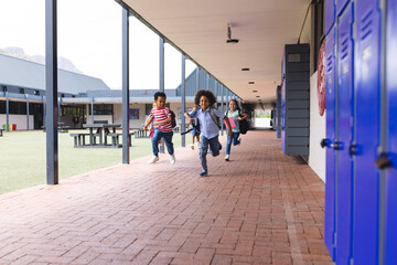In school, diverse children are running in the corridor with copy space outdoors