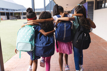 In school, four young girls are walking together outdoors, hugging each other