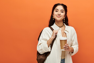 Young indian woman savoring a cup of coffee against an orange backdrop.