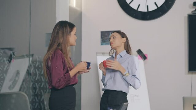 Indian Asian Hindu young adult busy gen z expert woman hold cup mug drink hot coffee enjoy fun joy talk gossip share news indoor job office teen age smiling female girls staff team have tea break time