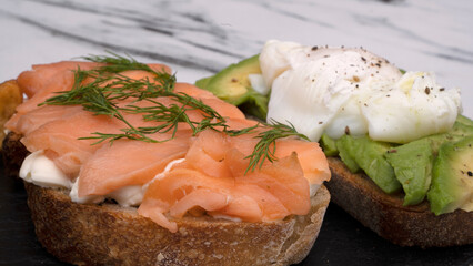 Healthy cuisine. Gourmet sandwich. Closeup view of a smoked salmon, cream cheese, sliced avocado and poached eggs sandwich in a black dish