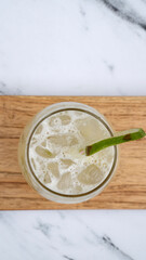 Tropical drinks. Top view of a Caipirinha cocktail with ice and lime on a wooden dish on a white marble table.