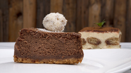 Sweet desserts. Closeup view of a chocolate cheesecake with a coconut truffle in the foreground and an Italian tiramisu with mascarpone cheese, coffee and vanilla biscuits slice in the background.