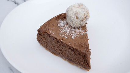 Sweet dessert. Closeup view of a slice of chocolate cheesecake with a coconut truffle, in a white plate.	
